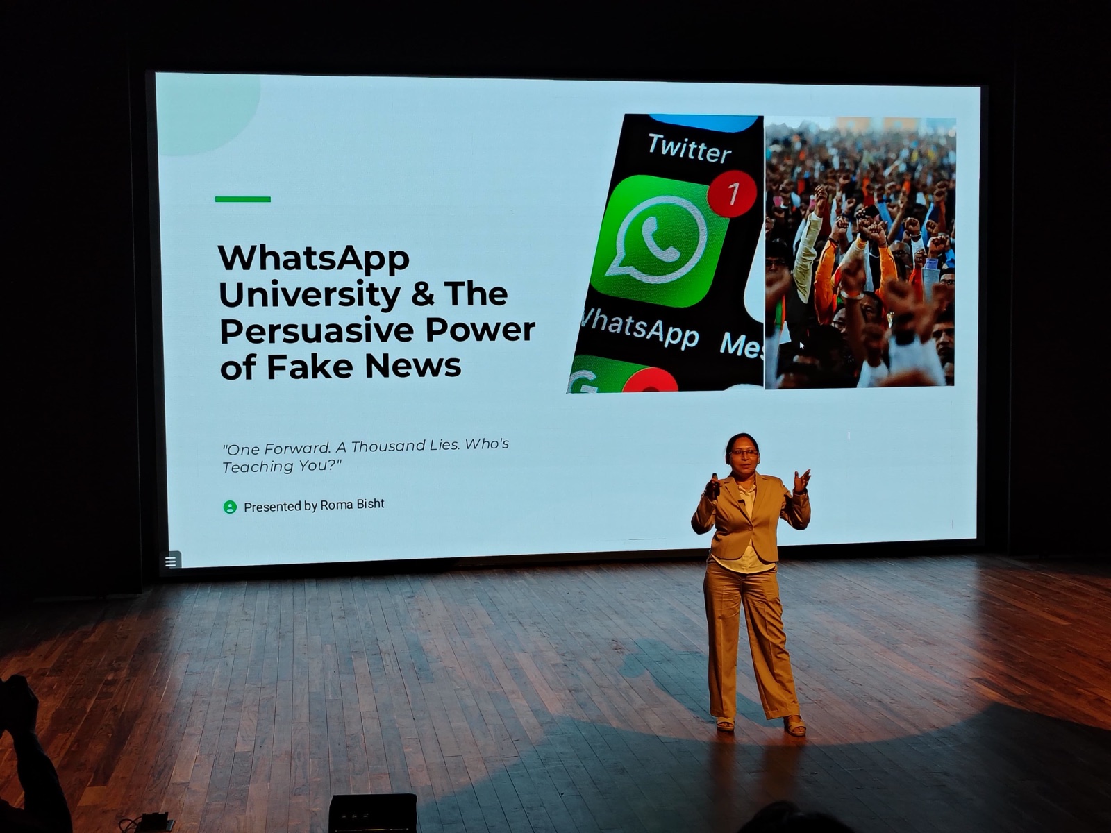 Roma Bisht presenting the WhatsApp University talk on stage, the title slide projected behind her